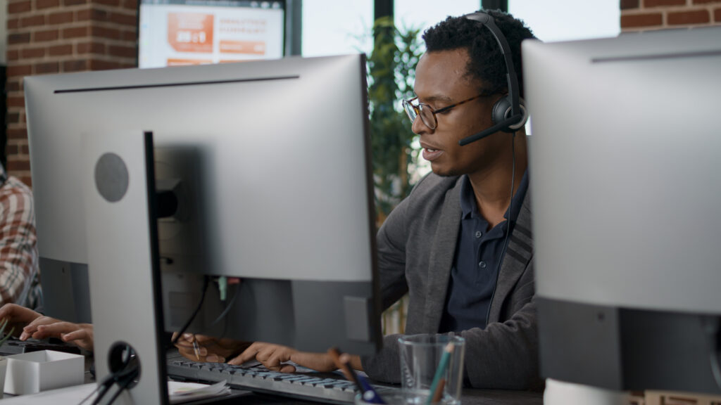 A headset-wearing support professional working at a desktop computer.