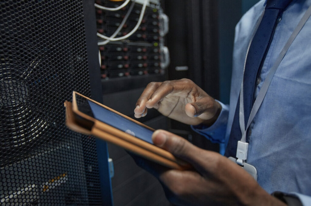 Close-up of a technician using a tablet beside server equipment.