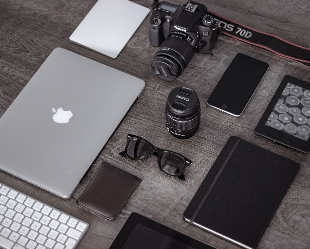 A laptop, tablet, phone and camera arranged neatly on a desk.